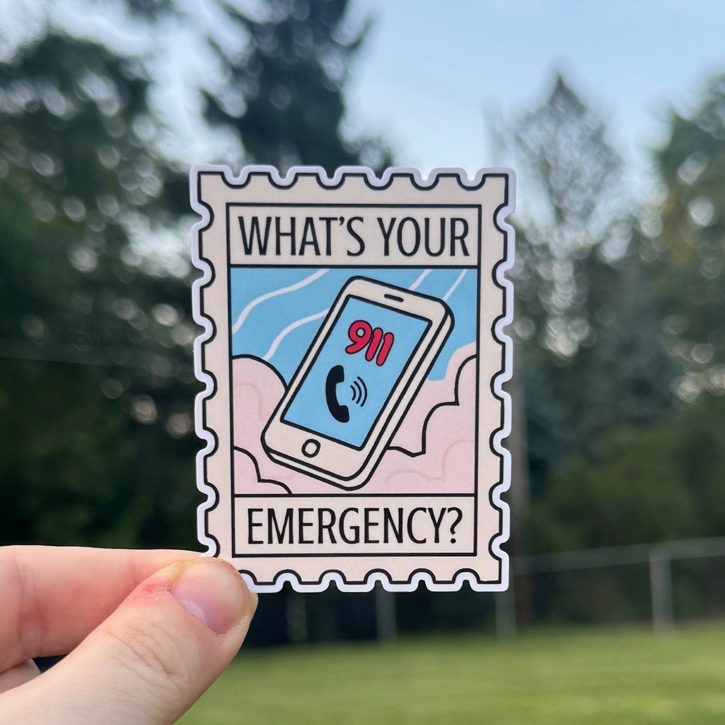 Hand holding a sticker with 'What's Your Emergency?' text against a blurred outdoor background