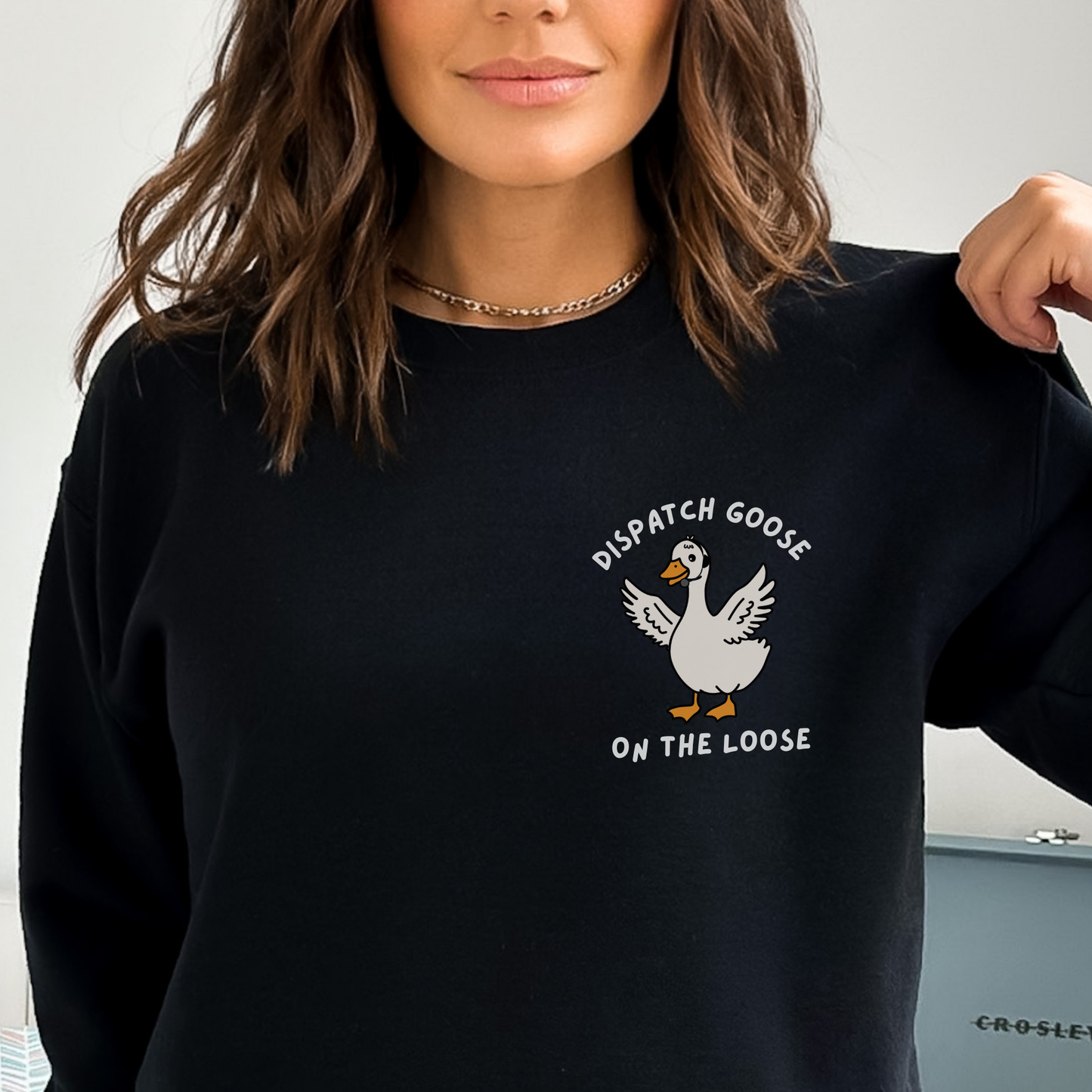 woman wearing a black crewneck with a dispatcher goose design over the left chest