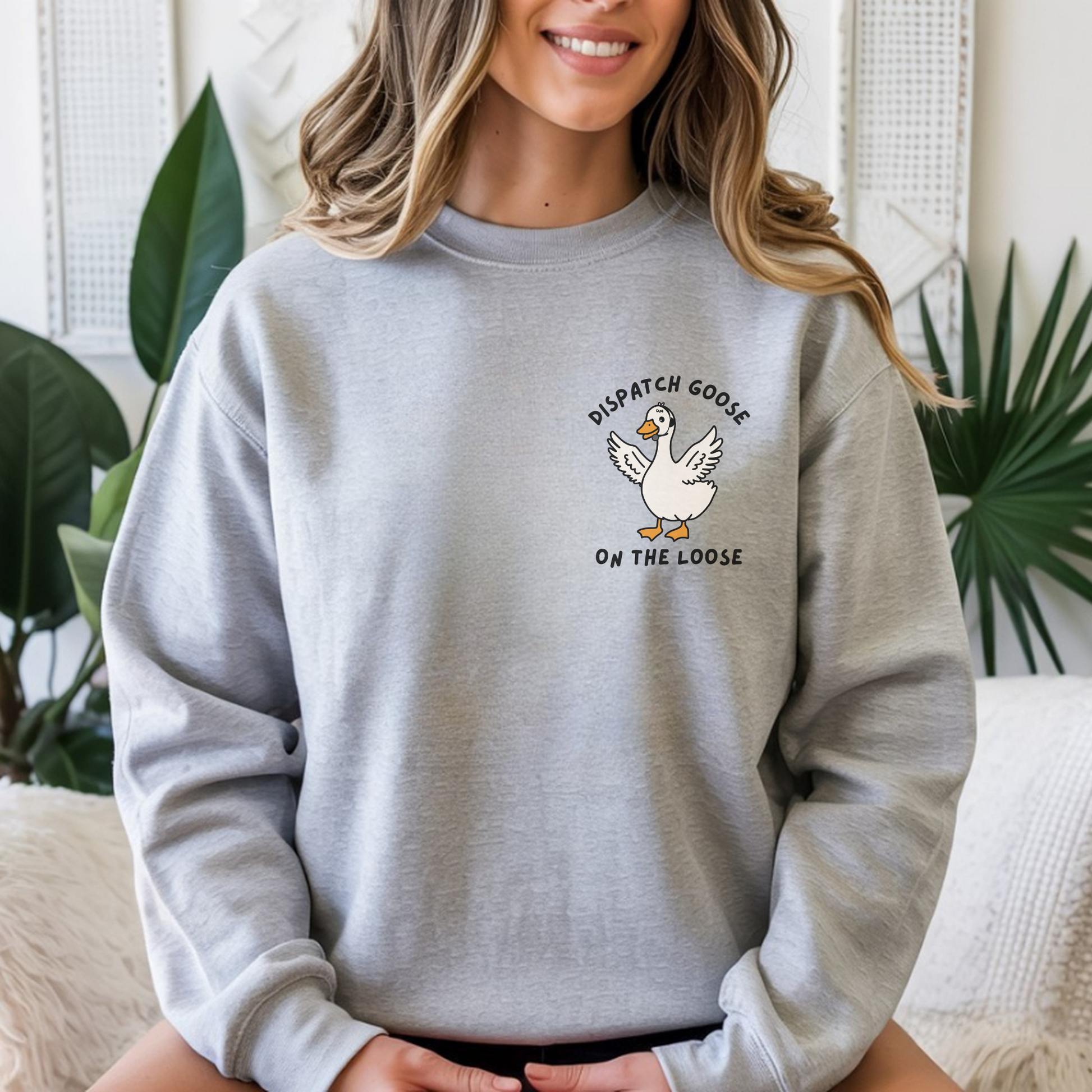 woman wearing an ash crewneck with a dispatcher goose design over the left chest