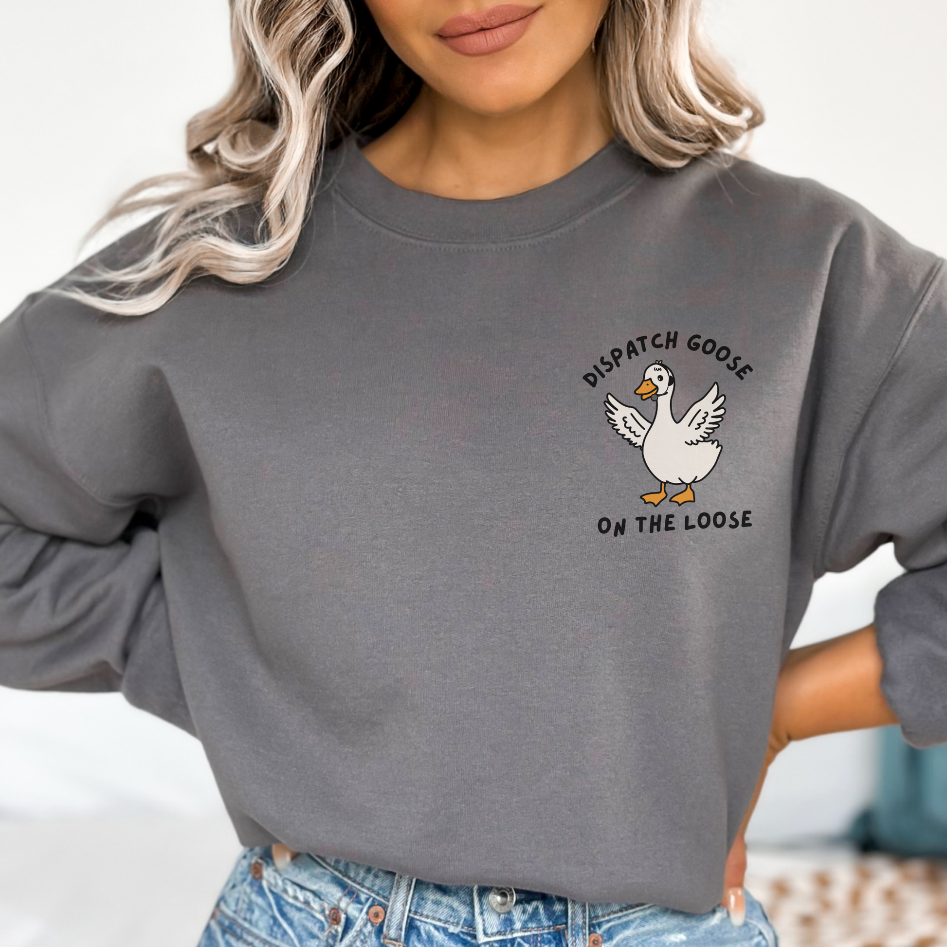 woman wearing a dark grey crewneck with a dispatcher goose design over the left chest
