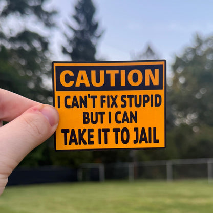 Hand holding a humorous 'Caution' sign with text outdoors.
