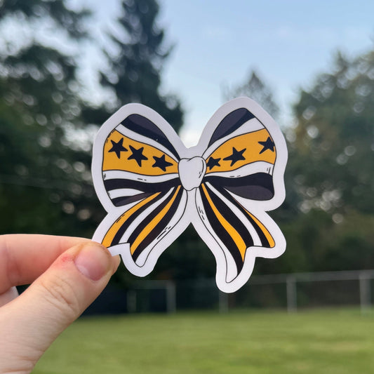 Hand holding a colorful bow-shaped sticker with a blurred outdoor background