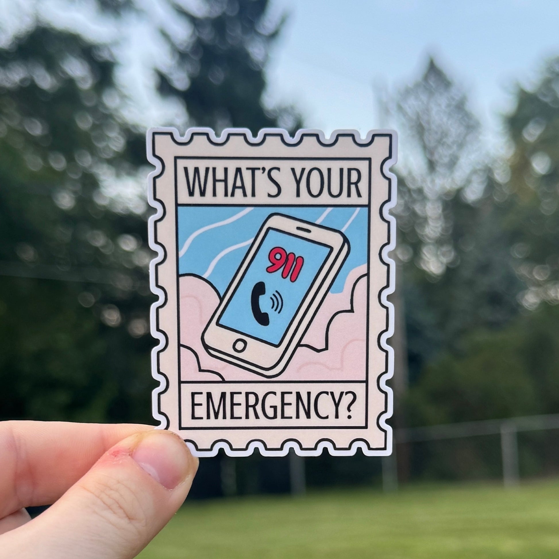 Hand holding a sticker with 'What's Your Emergency?' text against a blurred outdoor background