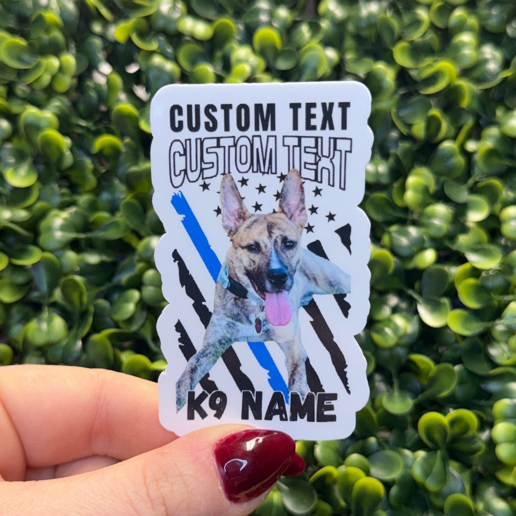 Hand holding a custom text and K9 name sticker against a green bush background