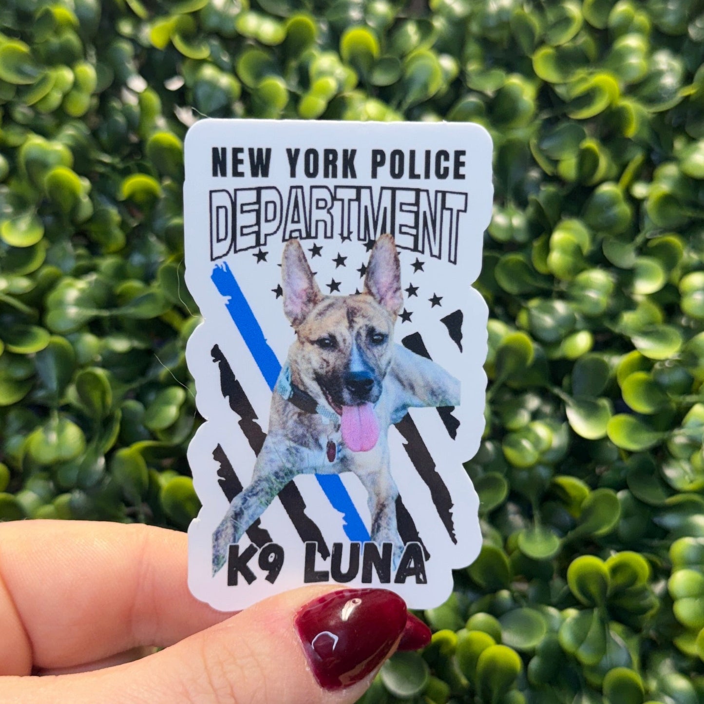 Sticker of a police dog held by a hand in front of green foliage