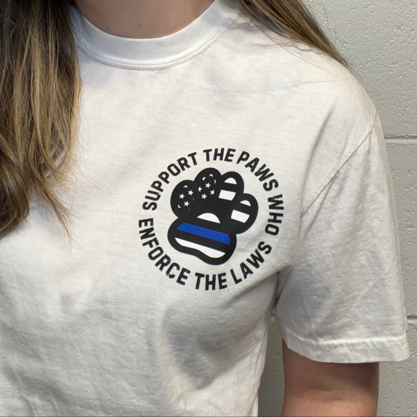 Person wearing a white t-shirt with a graphic and text against a light gray brick wall.