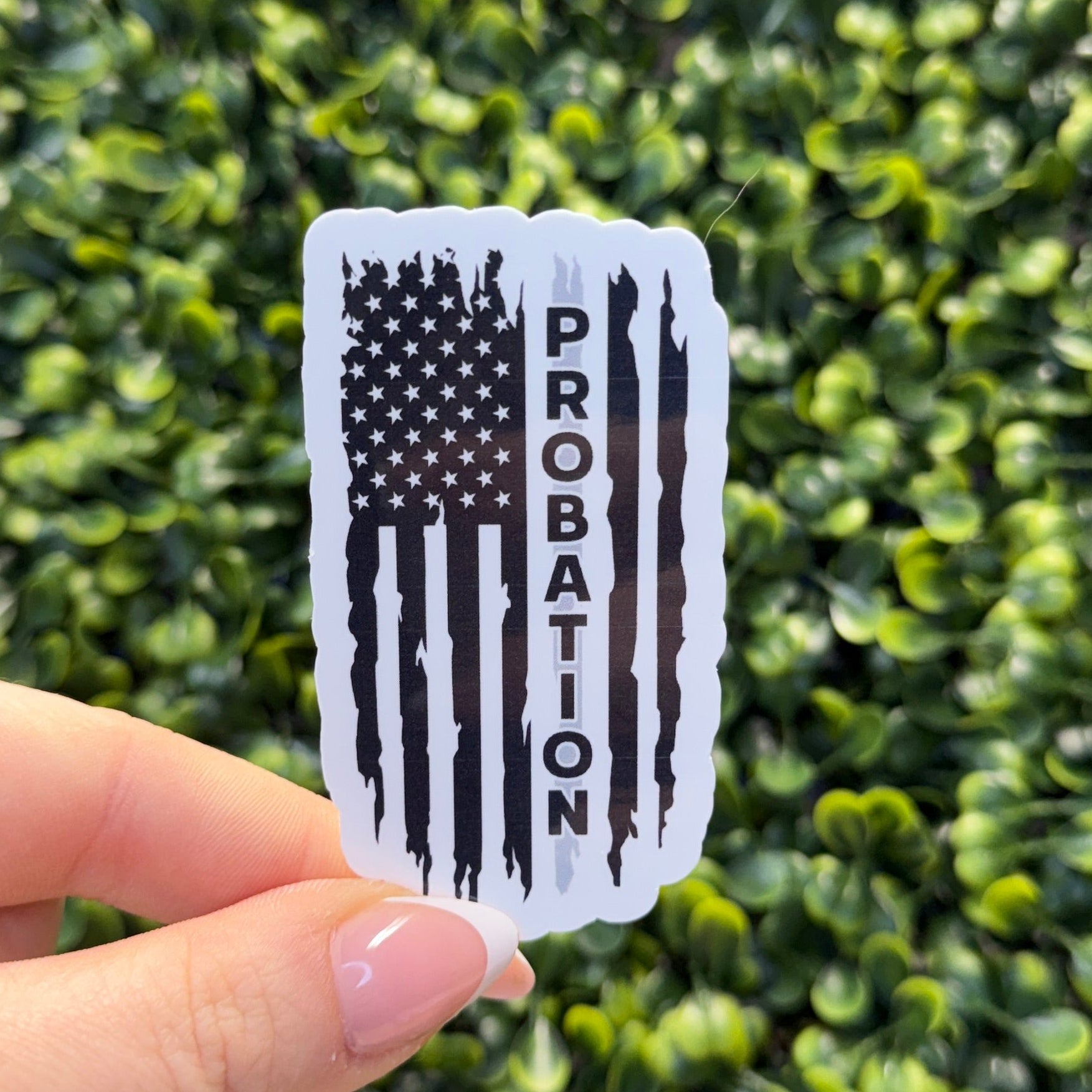 Hand holding a 'Probation' sticker with an American flag design against a green leafy background
