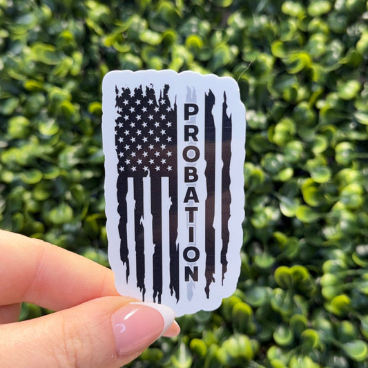 Hand holding a 'Probation' sticker with an American flag design against a green leafy background