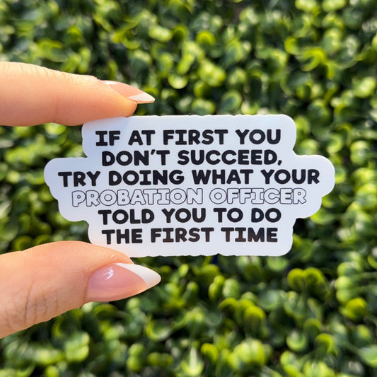 Hand holding a sticker with humorous text against a green hedge background