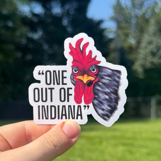 Hand holding a sticker with a rooster design and text outdoors